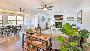 A spacious living room with a fireplace, a dining area with a wooden table and chairs, and a large window providing natural light. - Townville Lake House w/ Private Dock, Kayaks! (Townville)