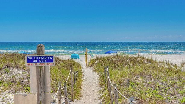 A beach path leading to the ocean with a sign warning 'NO LIFEGUARD ON DUTY. SWIM AT OWN RISK!'