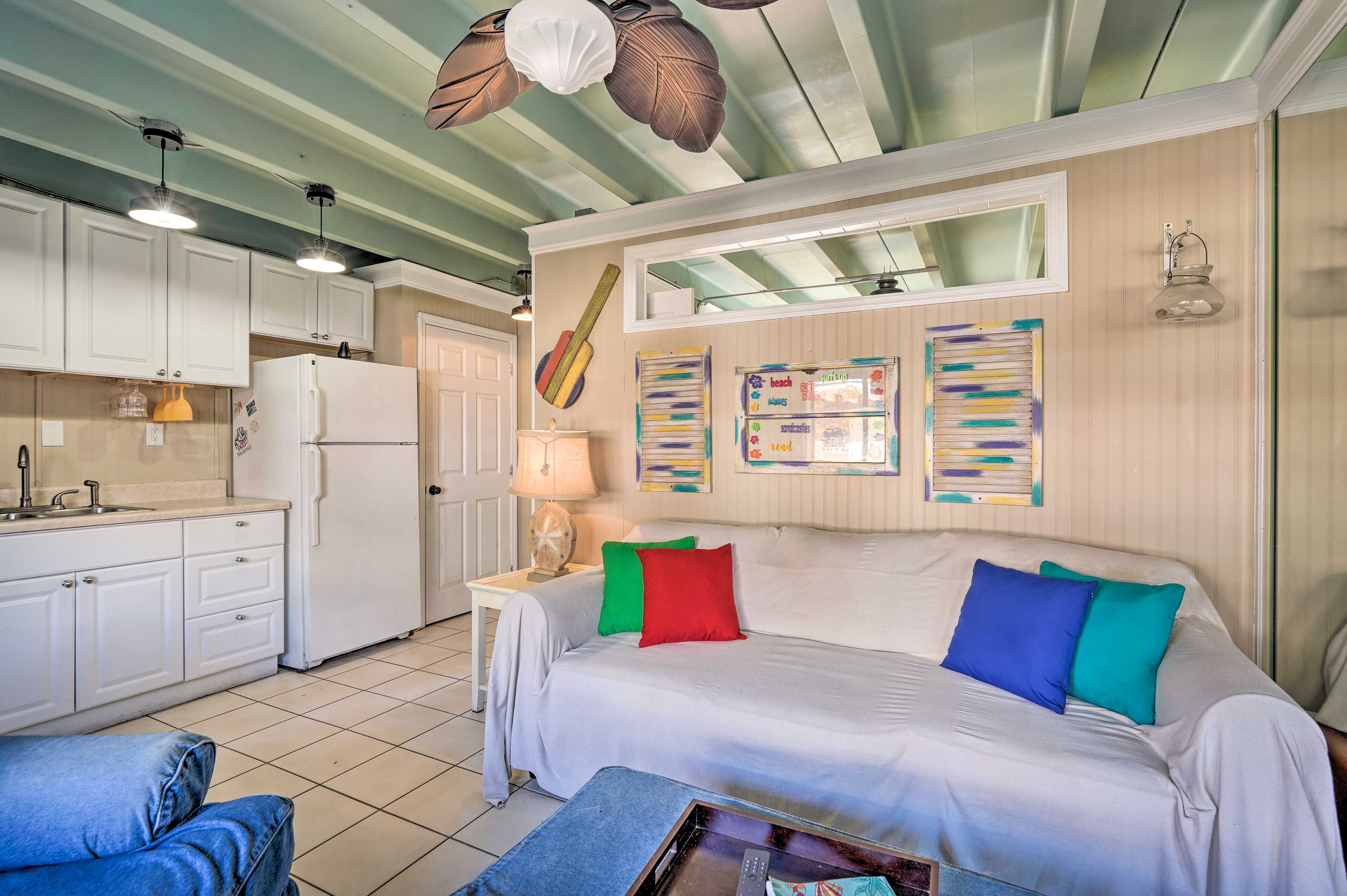 A compact room with a bed, a small table, a kitchenette, and a ceiling fan.