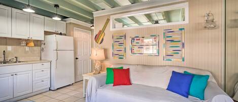 A compact room with a bed, a small table, a kitchenette, and a ceiling fan.