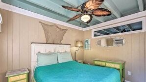 A bedroom with a bed, a nightstand, a dresser, a ceiling fan, a wall-mounted mirror, and a decorative wall piece.