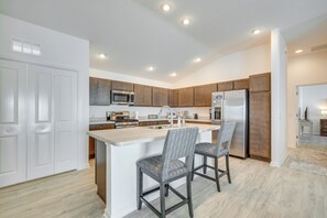 Una cocina moderna con armarios de madera, un refrigerador de acero inoxidable y una isla central con dos taburetes de bar.