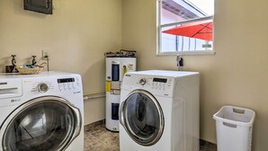 Ein Waschraum mit zwei Waschmaschinen mit Frontlader, einem Warmwasserbereiter und einem Mülleimer.