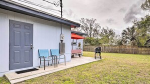 Ein Haus mit grauer Tür, einer überdachten Veranda mit einem roten Sonnenschirm und einem Grill im Garten.