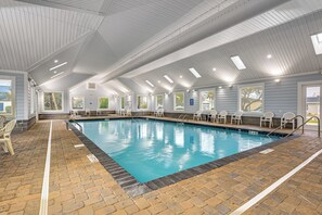 Una piscina interior con agua cristalina, rodeada de un suelo de ladrillo y sillas blancas.