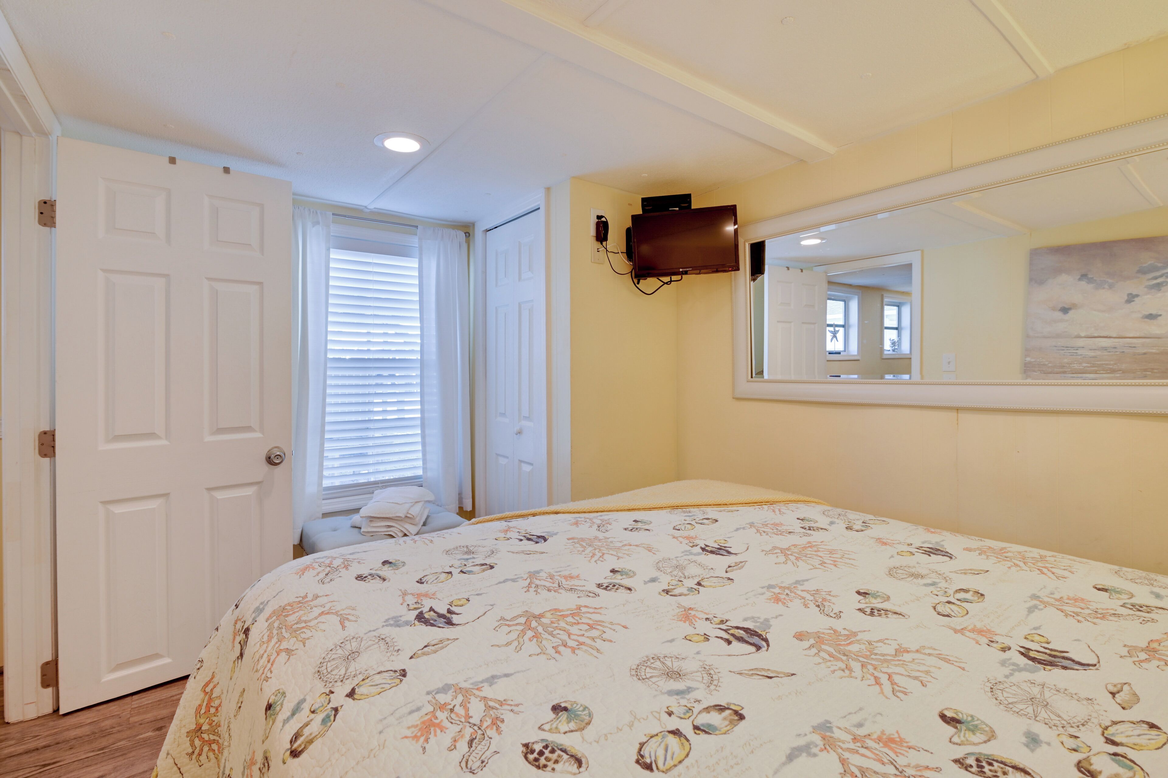 A bedroom with a bed, a door, a window with blinds, and a wall-mounted TV.