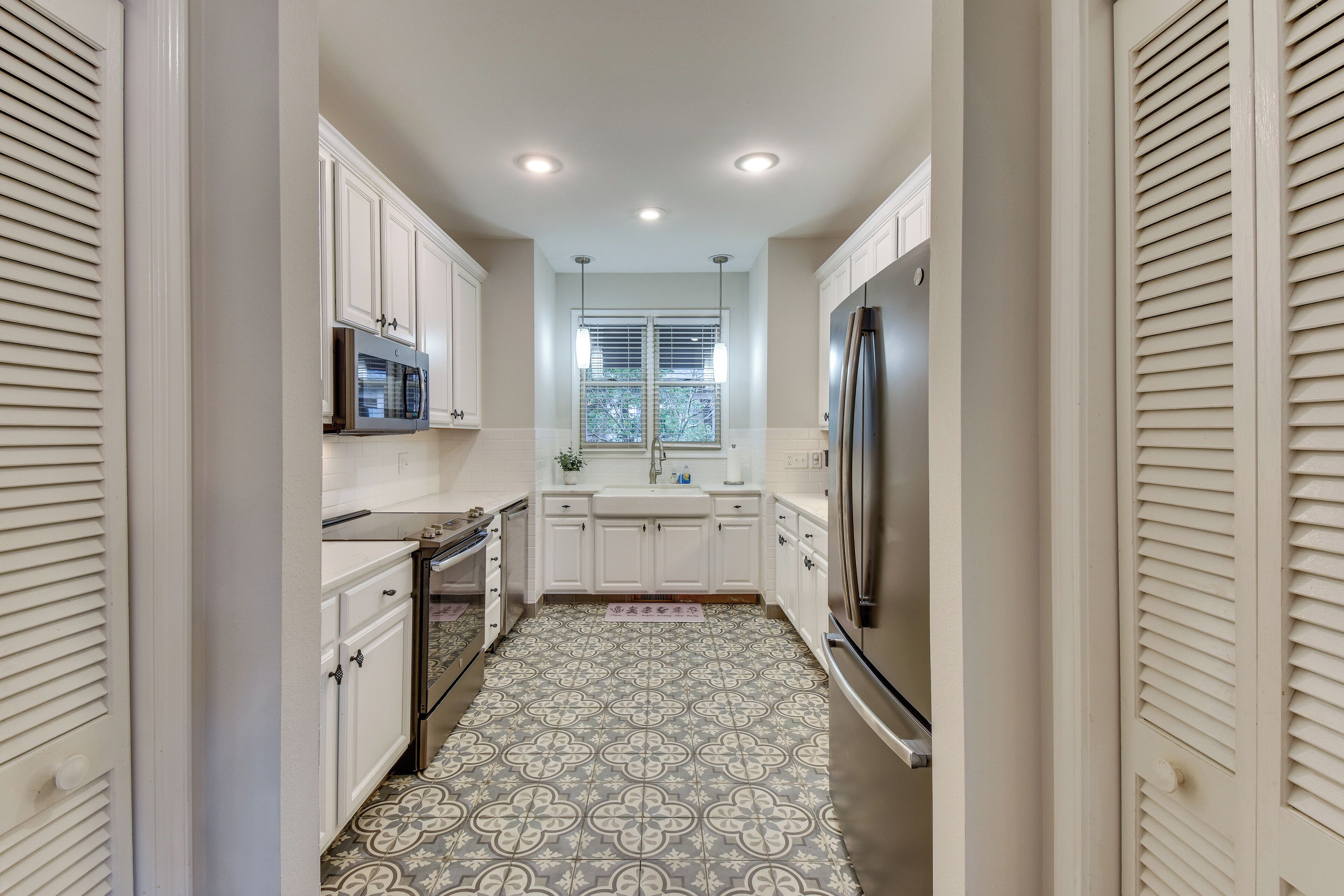 A narrow kitchen with white cabinets, a stainless steel refrigerator, and a microwave.