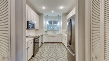 A narrow kitchen with white cabinets, a stainless steel refrigerator, and a microwave.