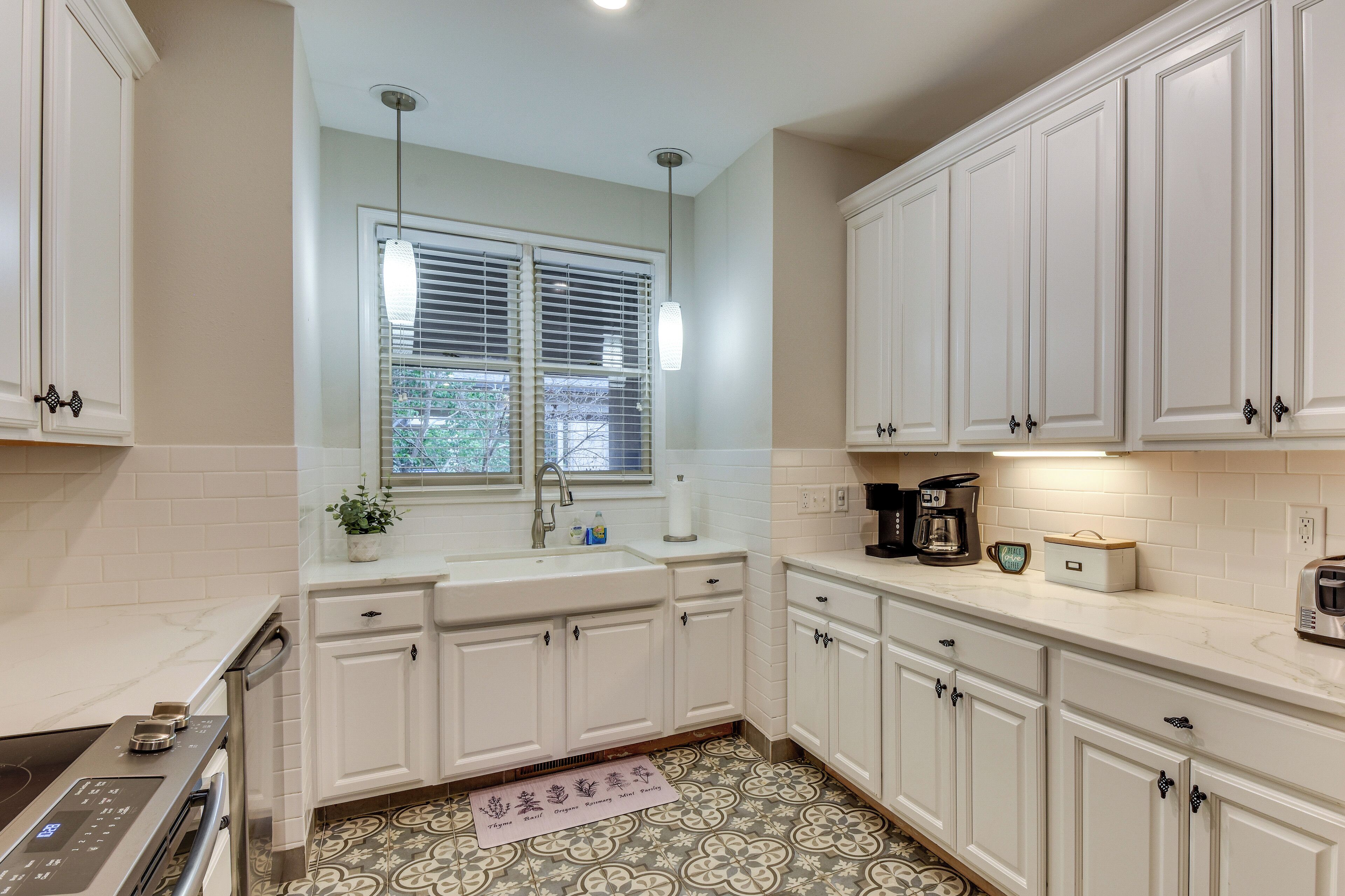 A kitchen with white cabinets, a window with blinds, a coffee maker, and a tea kettle.