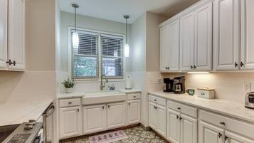 A kitchen with white cabinets, a window with blinds, a coffee maker, and a tea kettle.