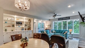 A well-lit room with a dining table, chairs, a sofa, and a large window with a view of trees. - Lake Keowee Resort Condo w/ Fantastic View (Salem)