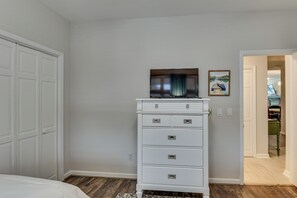 Une chambre avec une armoire blanche, un téléviseur à écran plat et un tableau accroché au mur.