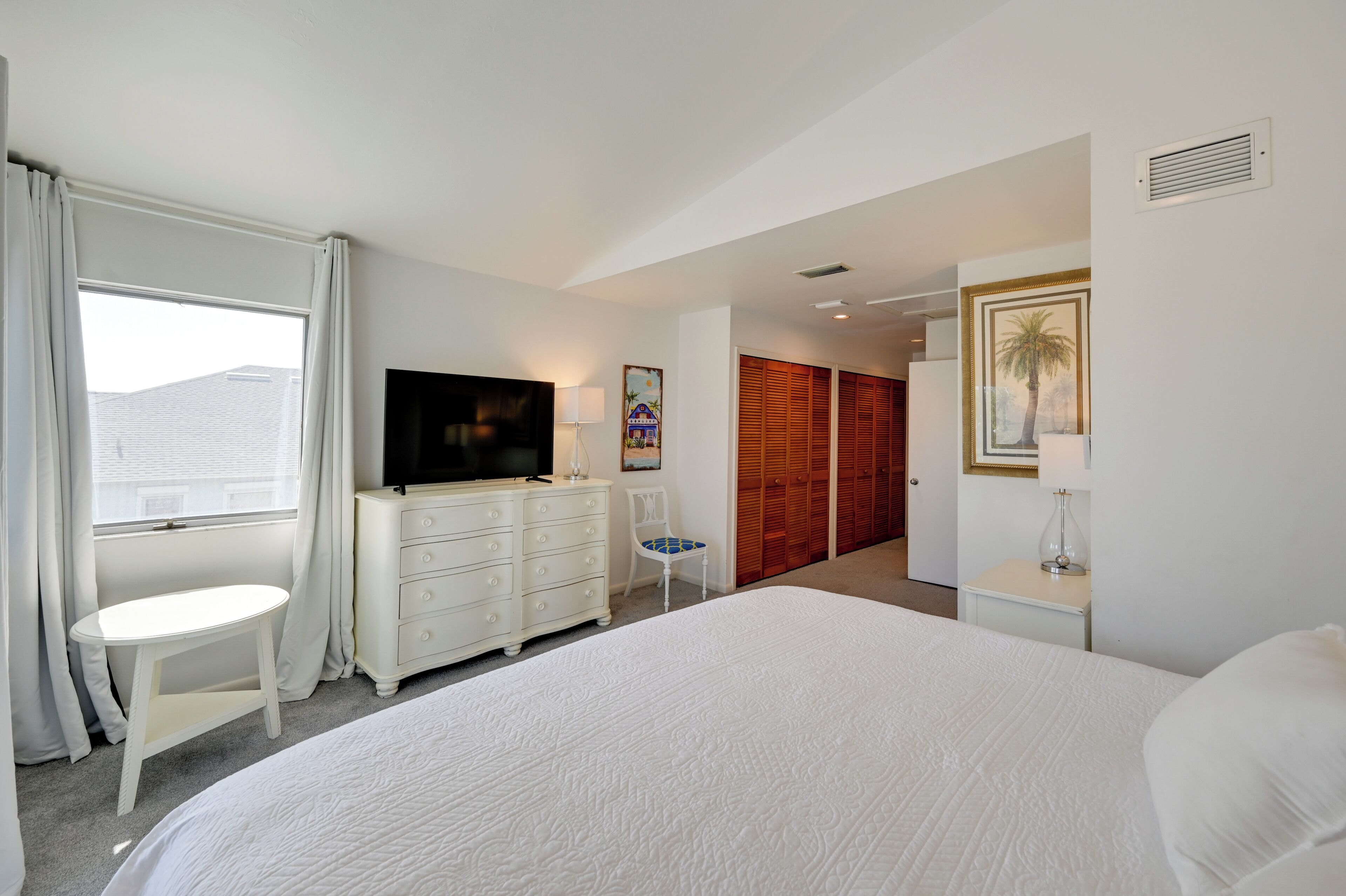 Una habitación de hotel con una cama grande, televisión, escritorio, silla y armario.