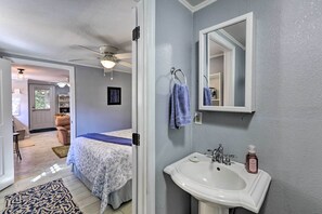 Une chambre avec un lit, une salle de bain avec un lavabo et un miroir, et un couloir menant à une autre pièce.