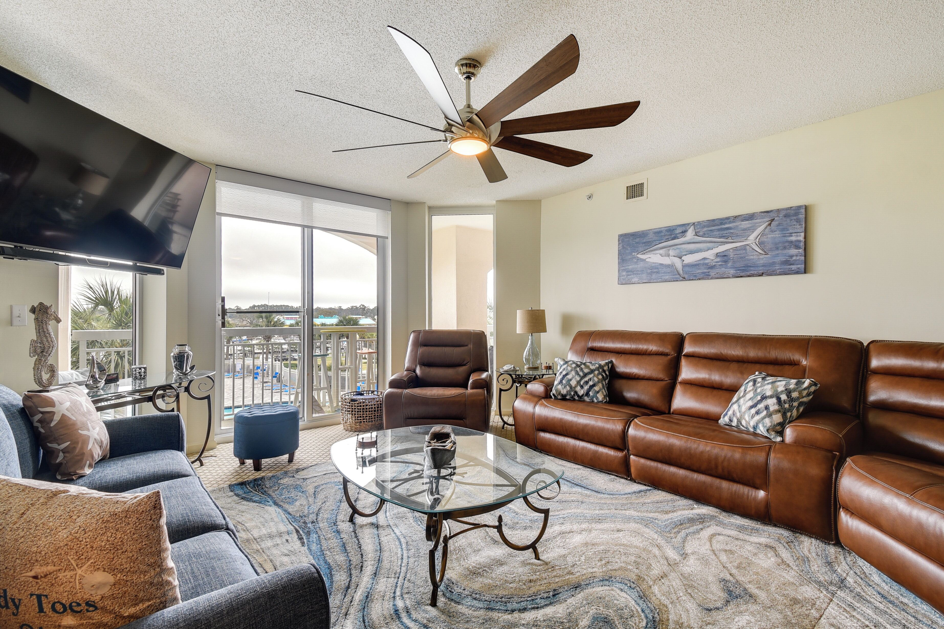 A living room with a brown leather sofa, a glass coffee table, and a ceiling fan.
