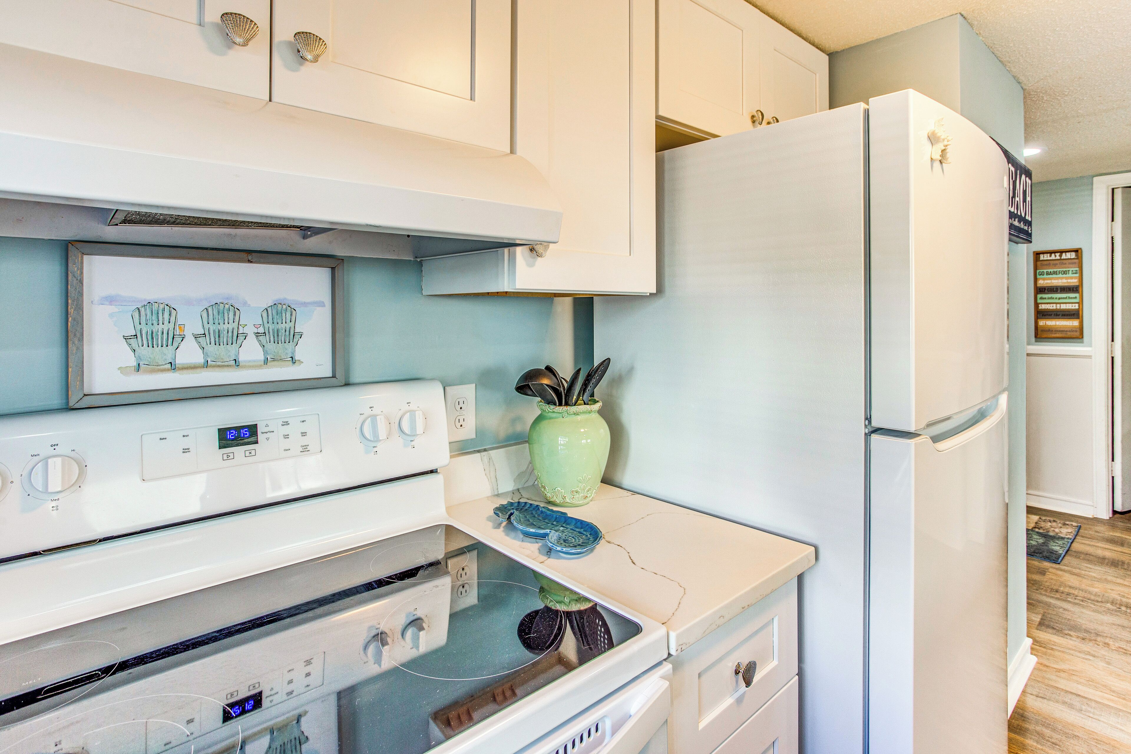 Una cucina con elettrodomestici bianchi, una cornice con una foto di sedie Adirondack e un vaso verde con utensili.