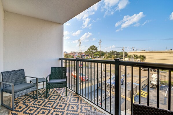 Un balcon avec deux chaises et une petite table, donnant sur un parking et une rue, avec des bâtiments en arrière-plan.