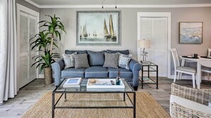 Uma sala de estar com sofá, mesa de centro e uma pintura de barcos à vela.