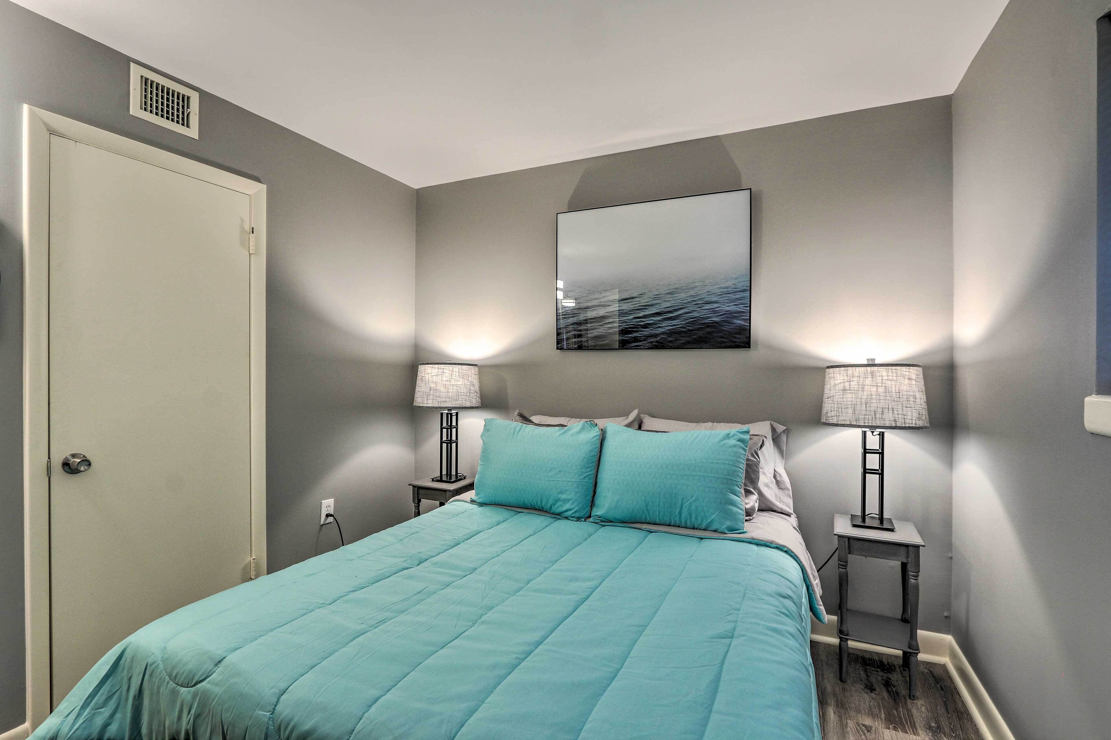 A bedroom with a bed, two bedside lamps, a wall-mounted picture, and a door.