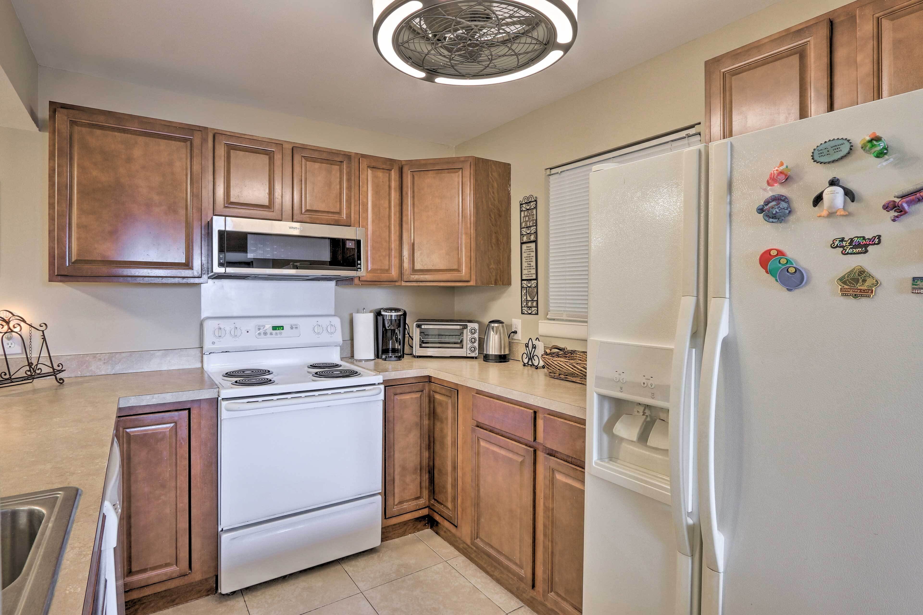 A kitchen with wooden cabinets, a white stove, a microwave, a refrigerator, and various kitchen appliances.