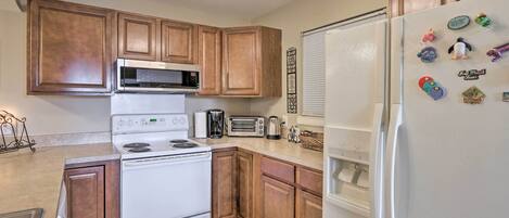 A kitchen with wooden cabinets, a white stove, a microwave, a refrigerator, and various kitchen appliances.