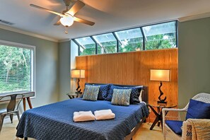 A bedroom with a large bed, two bedside lamps, a ceiling fan, and a window with a view of greenery. - Updated Hilton Head Condo: Balcony, Walk to Beach (Hilton Head Island)