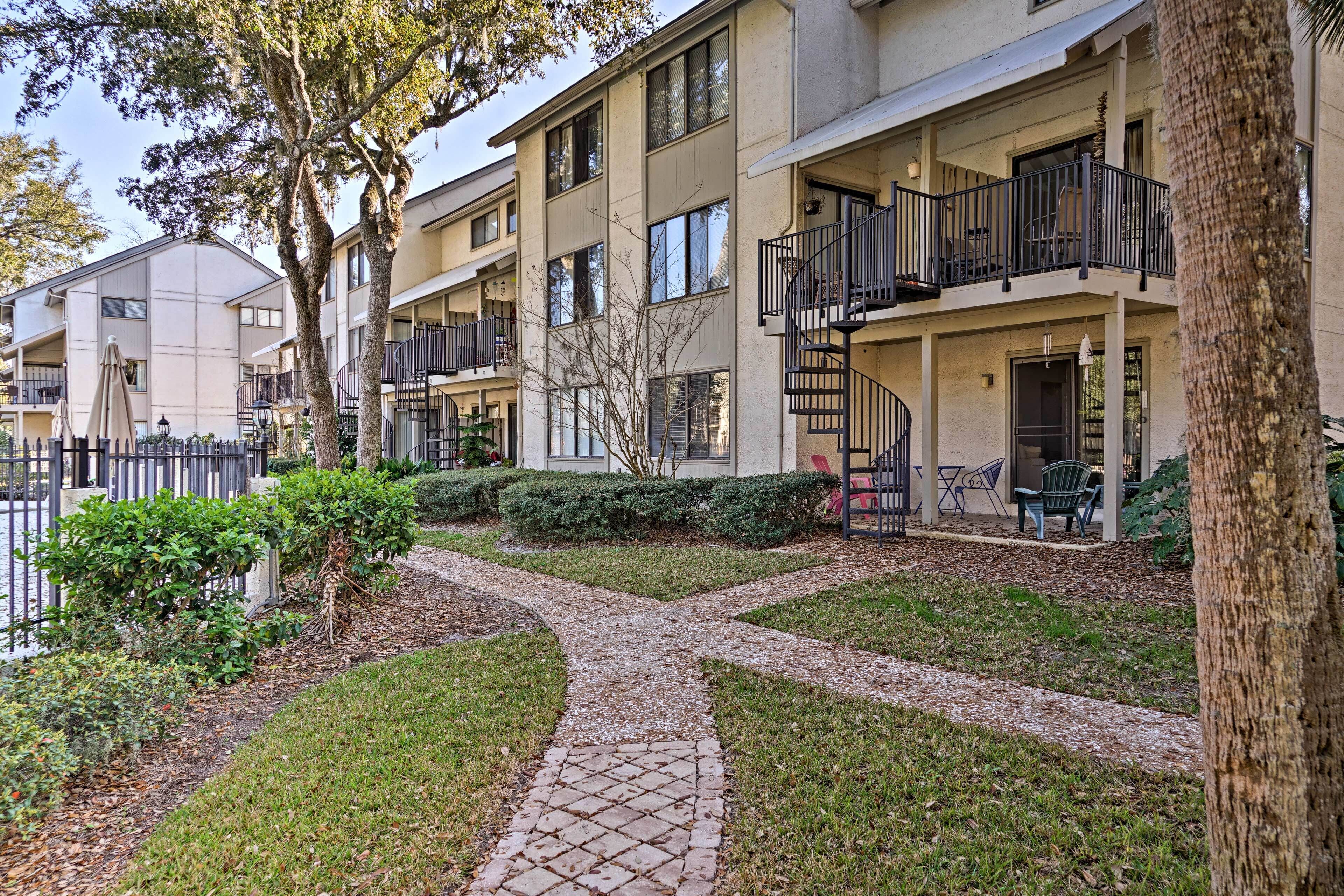 A multi-story residential building with balconies, a paved walkway, and surrounding greenery.
