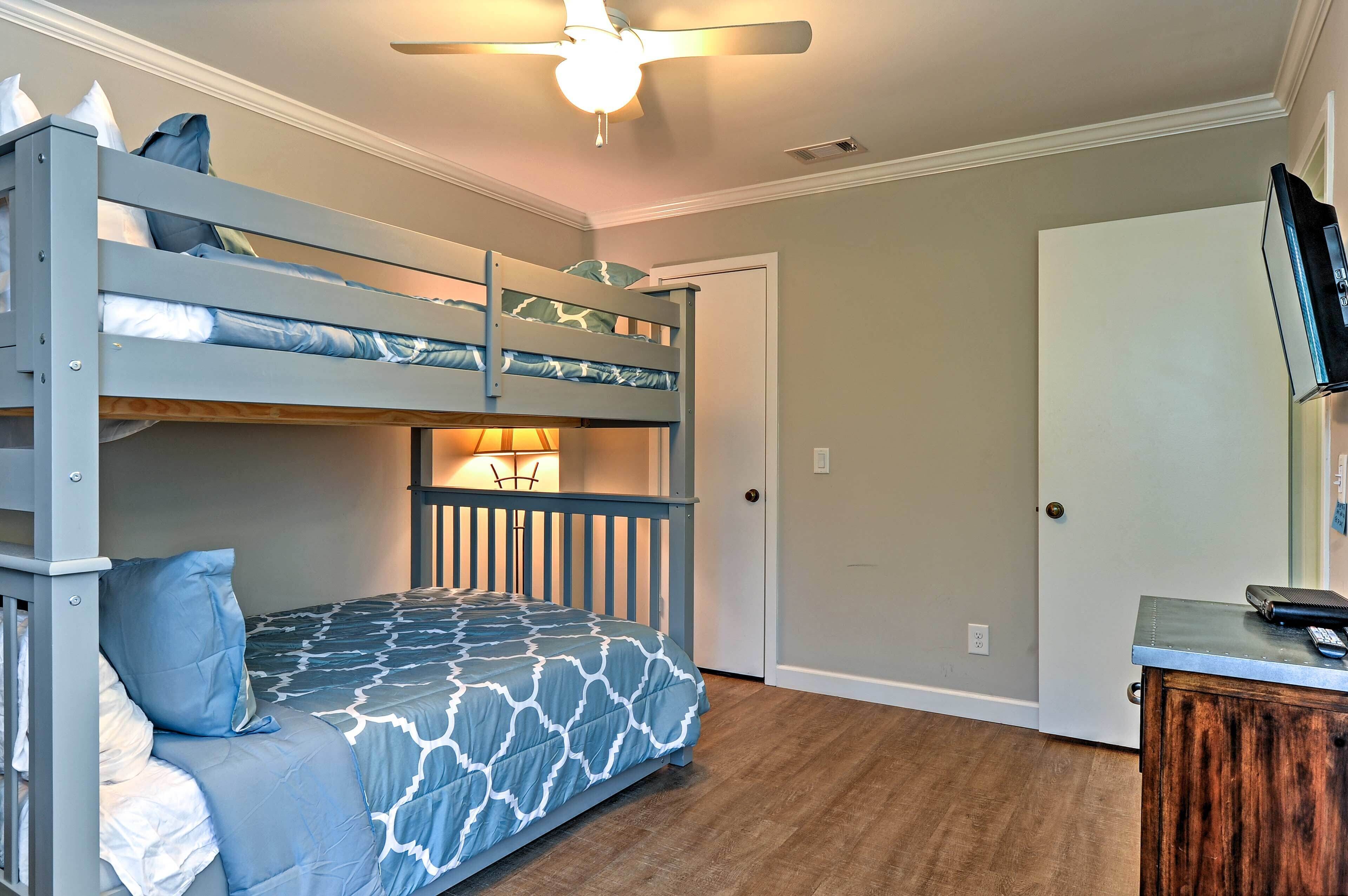 A bunk bed room with a ceiling fan, a desk with a lamp, and a door.