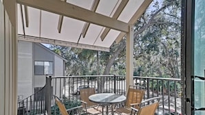 Un espace extérieur abrité, doté d’une table et de chaises, d’une rambarde et offrant une vue sur des arbres et un bâtiment.