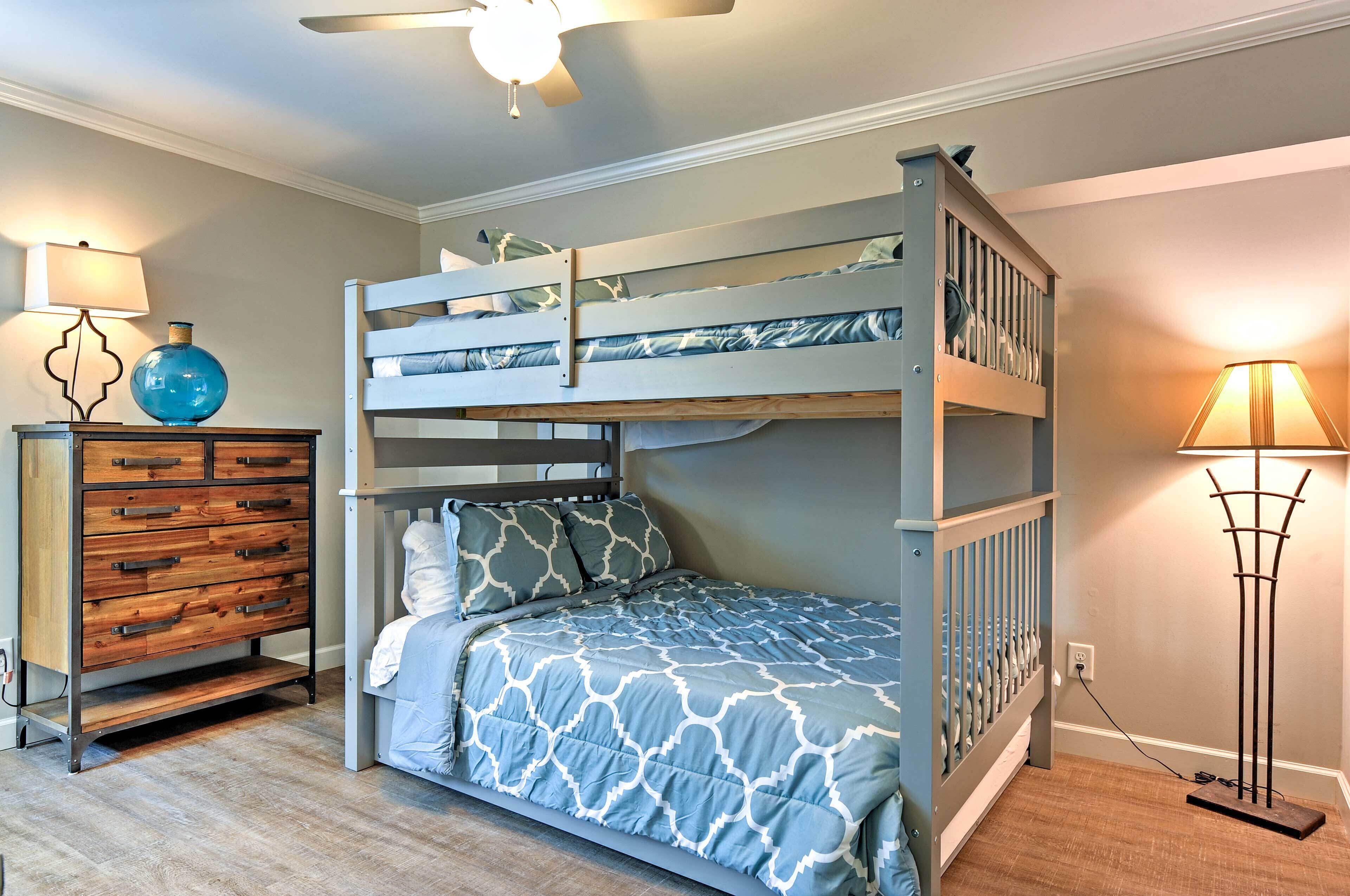 A bunk bed with a patterned bedspread, a wooden dresser with drawers, and a floor lamp.