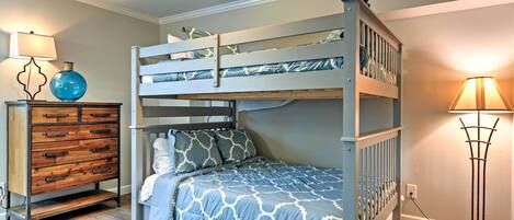 A bunk bed with a patterned bedspread, a wooden dresser with drawers, and a floor lamp.