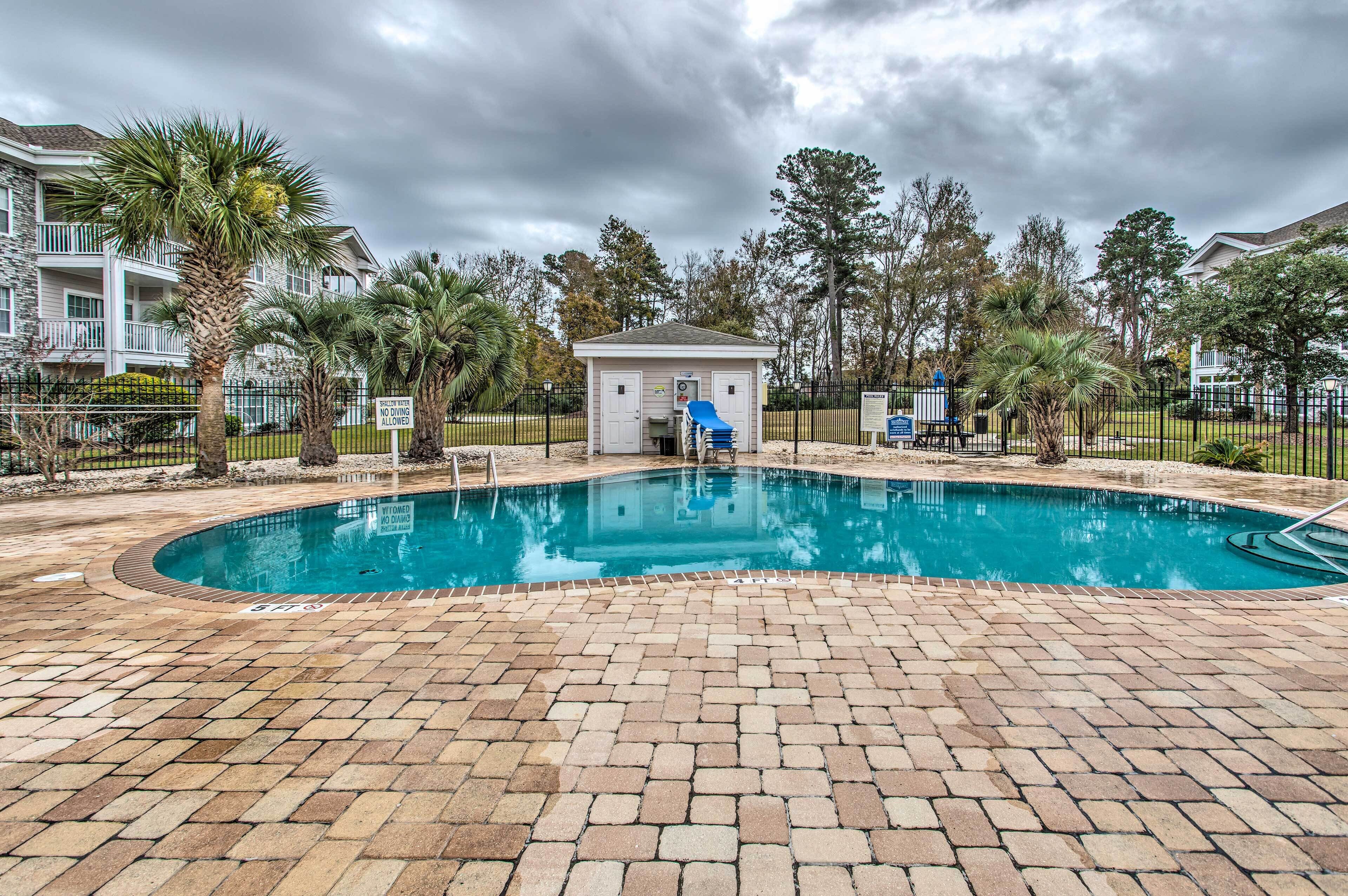 A swimming pool with a small building in the center, surrounded by palm trees and a fence.