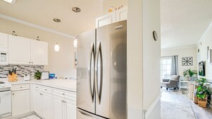 A modern kitchen with white cabinets, a stainless steel refrigerator, and a dining area with a gray sofa and a coffee table. - Pools & Golf, 2 Mi to Beach: Myrtle Beach Condo! (Myrtle Beach)