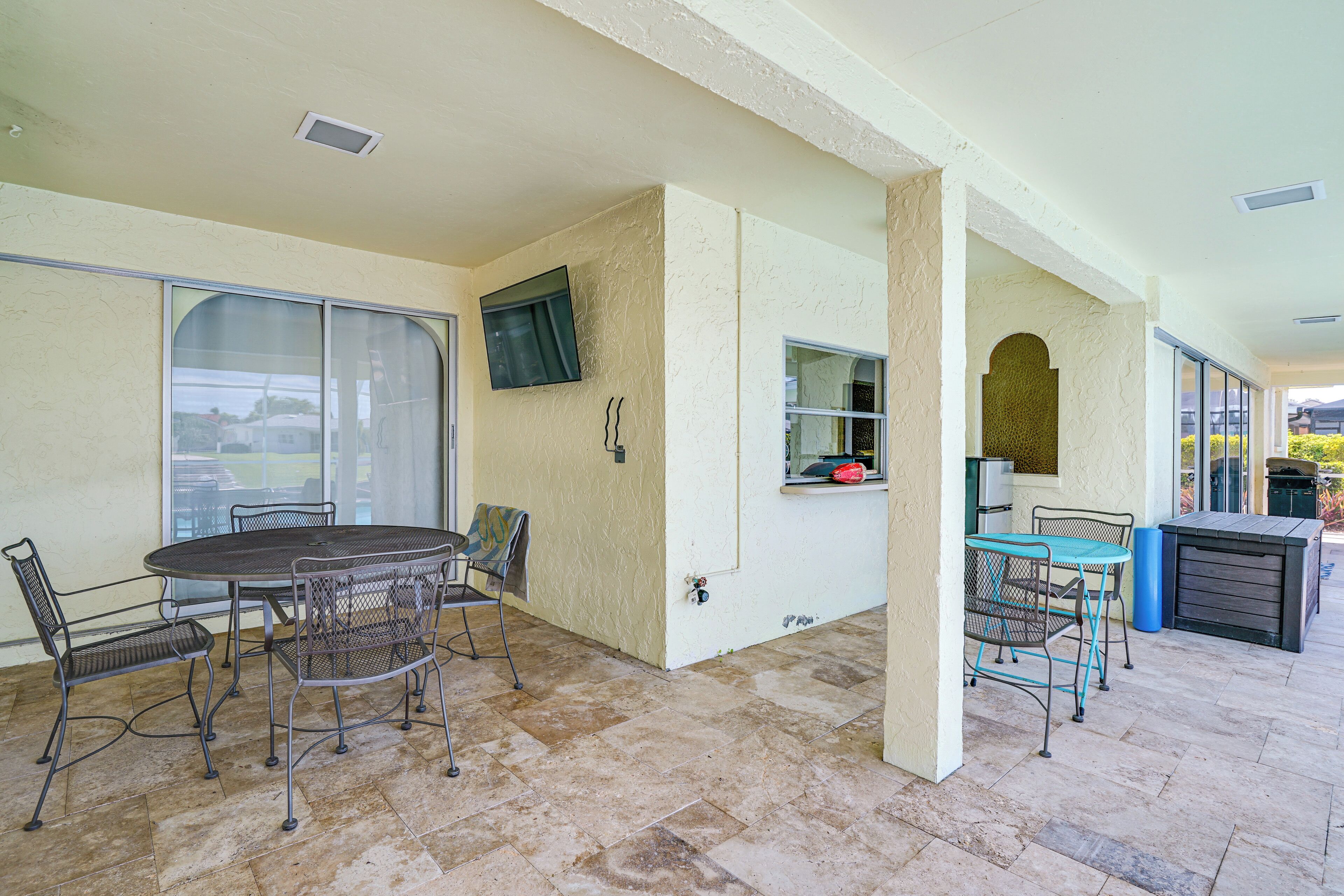An outdoor patio area with a round table and chairs, a TV mounted on the wall, and a grill station.