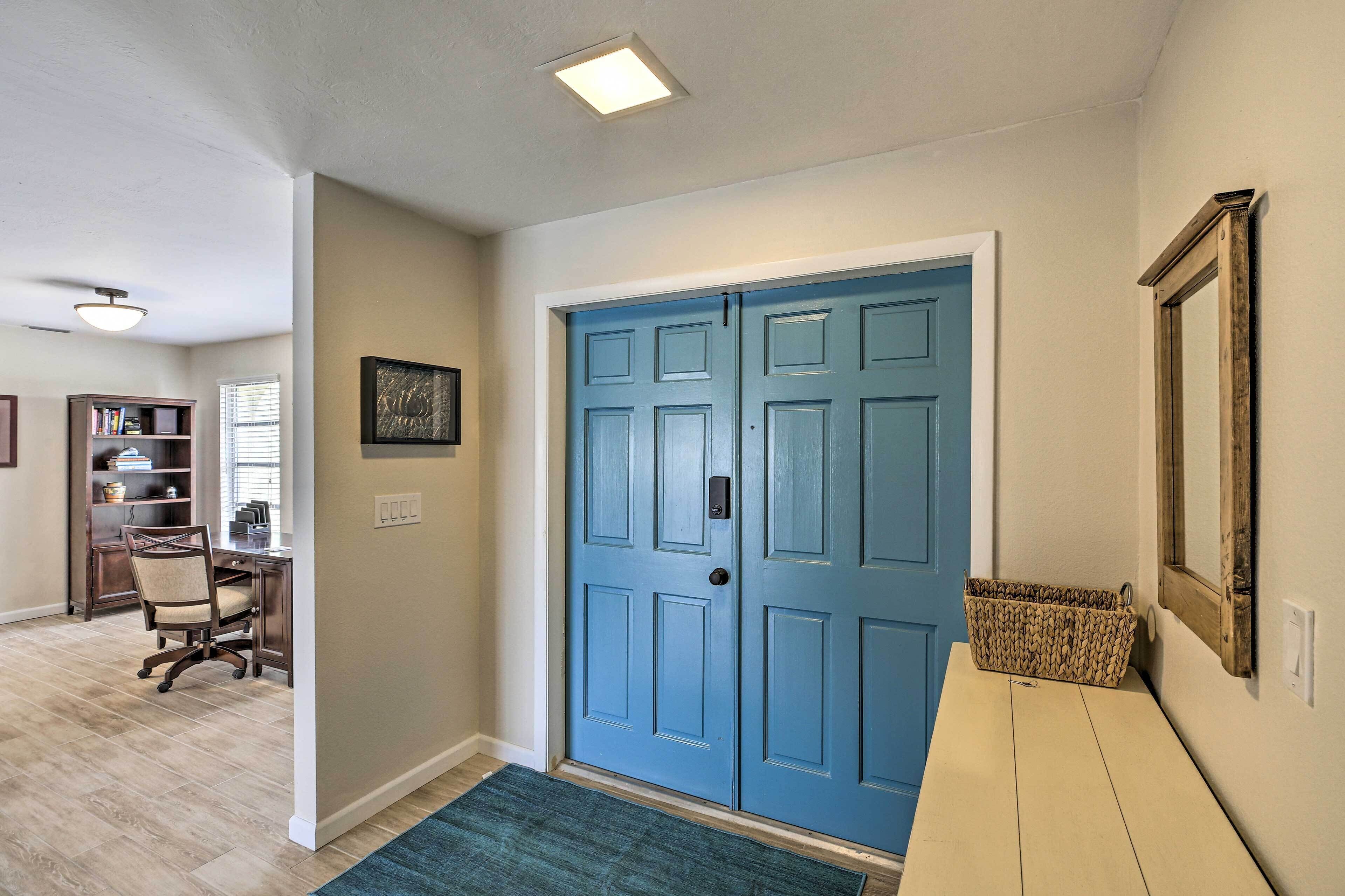 A room with a blue door, a desk with a chair, a bookshelf, and a window with blinds.