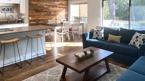 Eine moderne Küche mit einer Wandpaneinung aus Holz, einem Essbereich mit weißen Stühlen und einem blauen Sofa mit gemusterten Kissen.