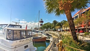 Eine Marina mit vertäuten Booten, ein Leuchtturm im Hintergrund und eine Palme im Vordergrund.