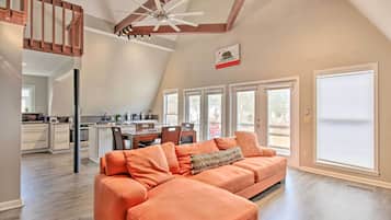 A spacious living area with a large orange sectional sofa, a ceiling fan, and a kitchen in the background.