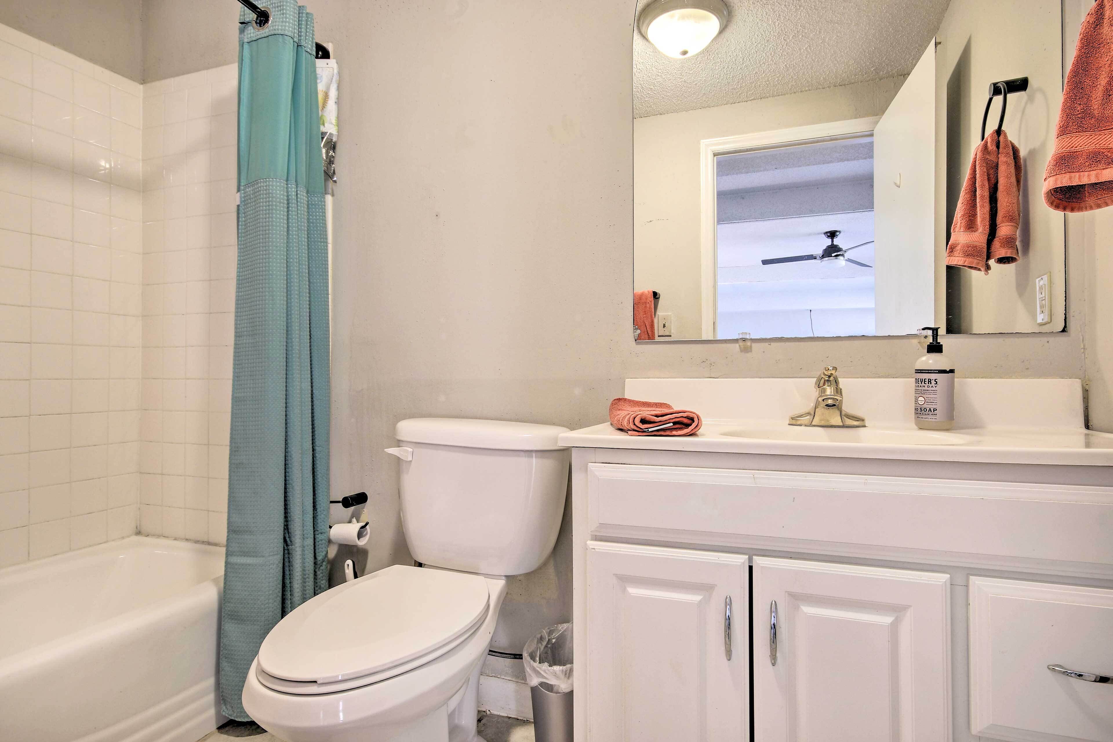 Une salle de bain comprenant des toilettes, une baignoire, un rideau de douche, un lavabo avec un miroir et un porte-serviettes.