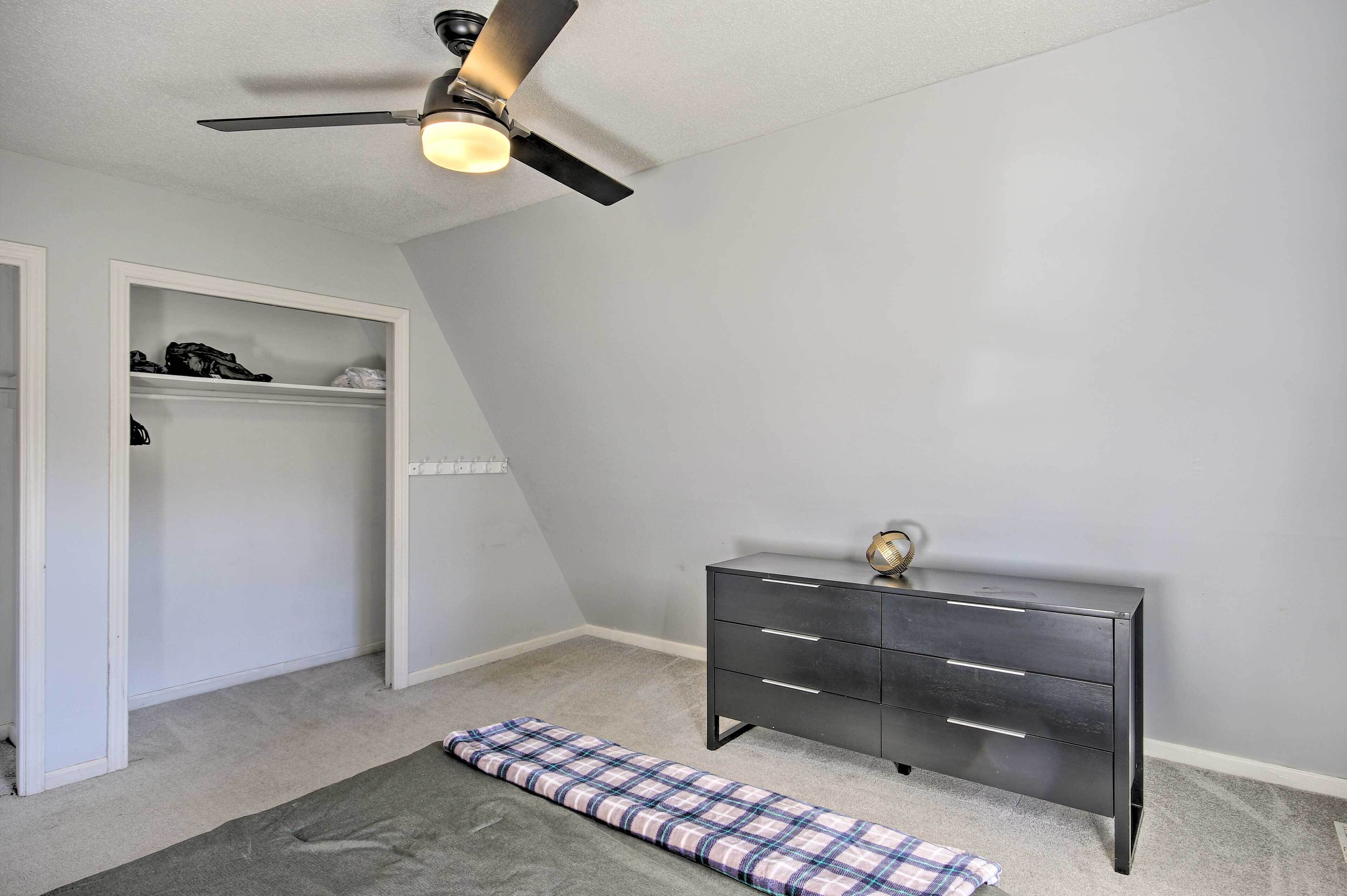 A bedroom with a ceiling fan, a dark dresser, a plaid bed runner, and a closet with shelves.