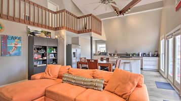 A spacious living area with a large orange sectional sofa, a wooden staircase, and a modern kitchen in the background.