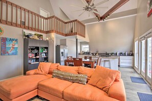 A spacious living area with a large orange sectional sofa, a wooden staircase, and a modern kitchen in the background. - Waterfront Chapin Home w/ Private Dock! (Chapin)