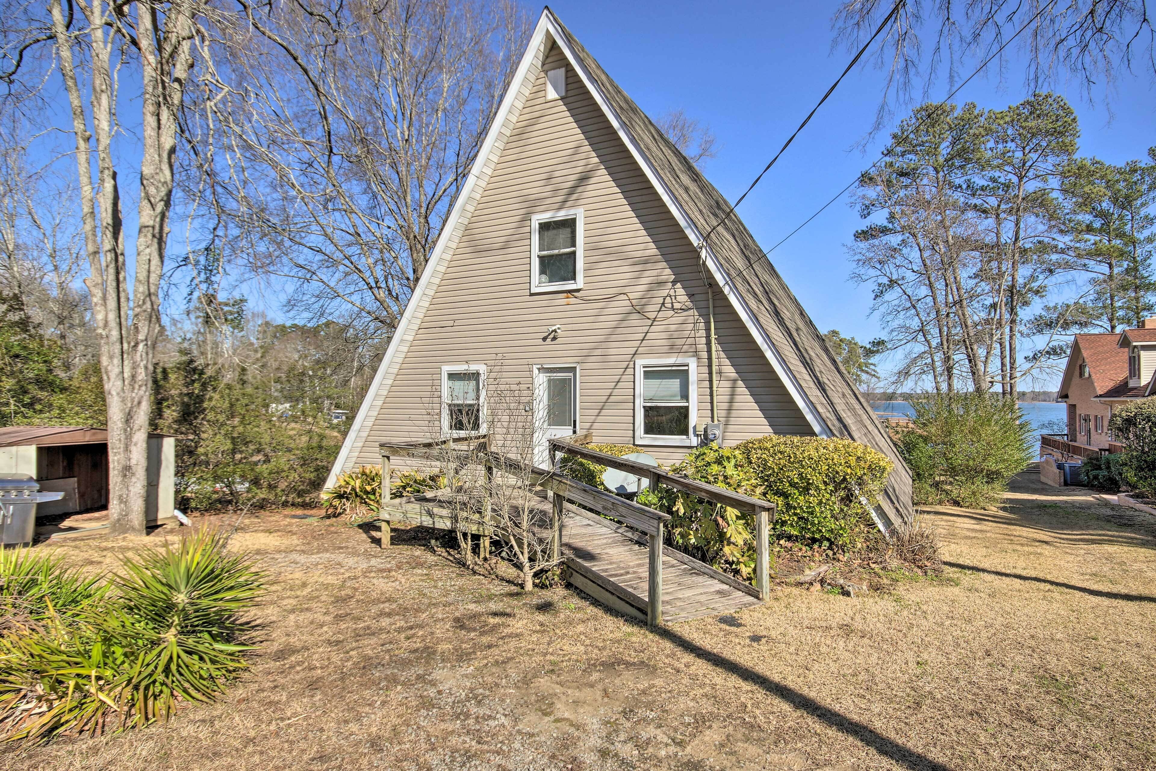 Une maison triangulaire dotée d’une terrasse en bois et d’un petit pont menant à la porte d’entrée.