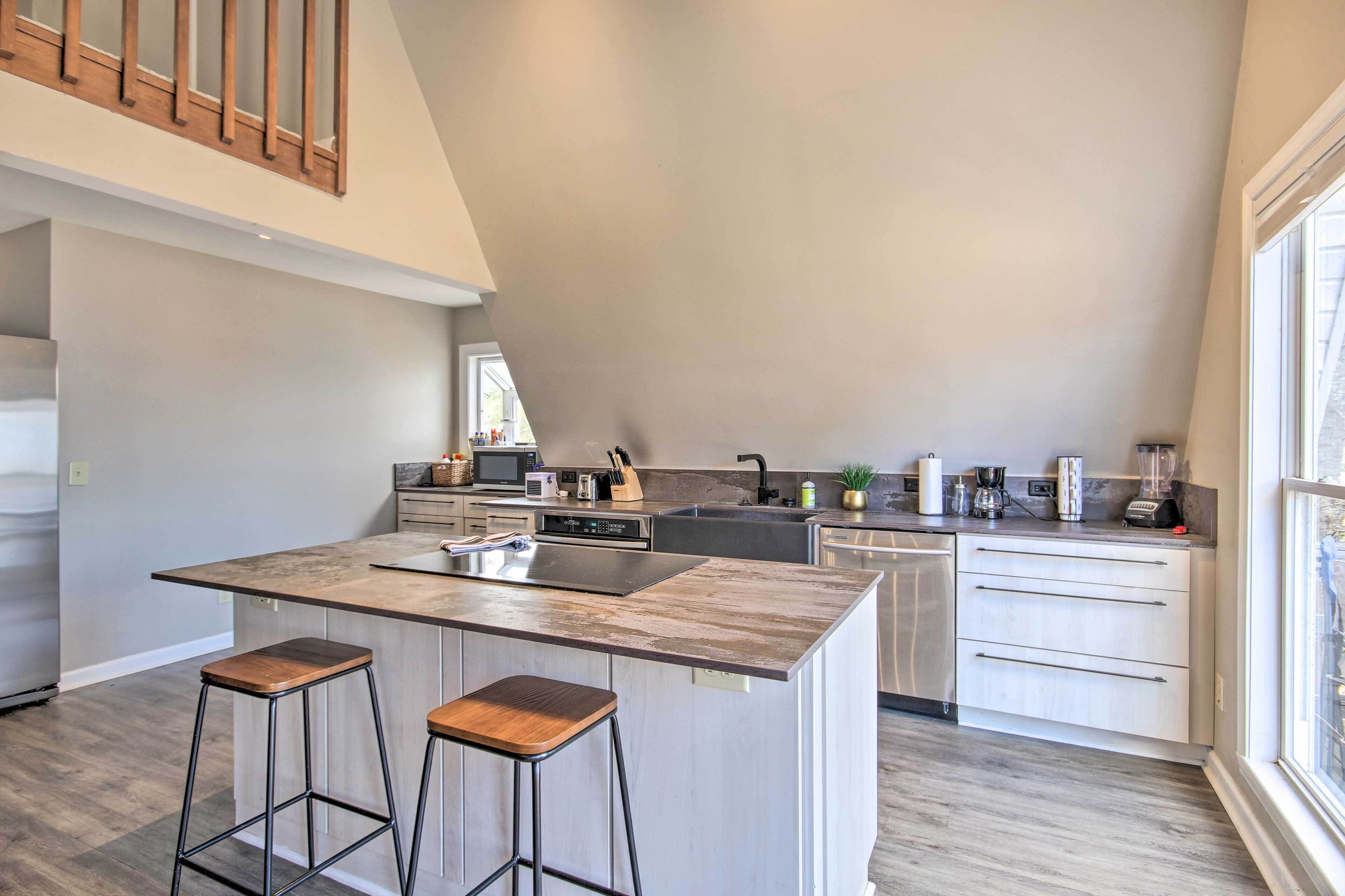 A modern kitchen with a central island, bar stools, stainless steel appliances, and a large window providing natural light.