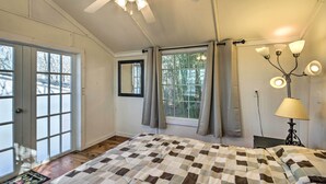Un dormitorio con una cama grande, un ventilador de techo, una ventana con cortinas y una mesita de noche con una lámpara.