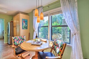 A dining area with a wooden table, two chairs with floral upholstery, a refrigerator, and a window with curtains. - Vibrant Rockledge Home ~ 2 Mi to Cocoa Village! (Rockledge)