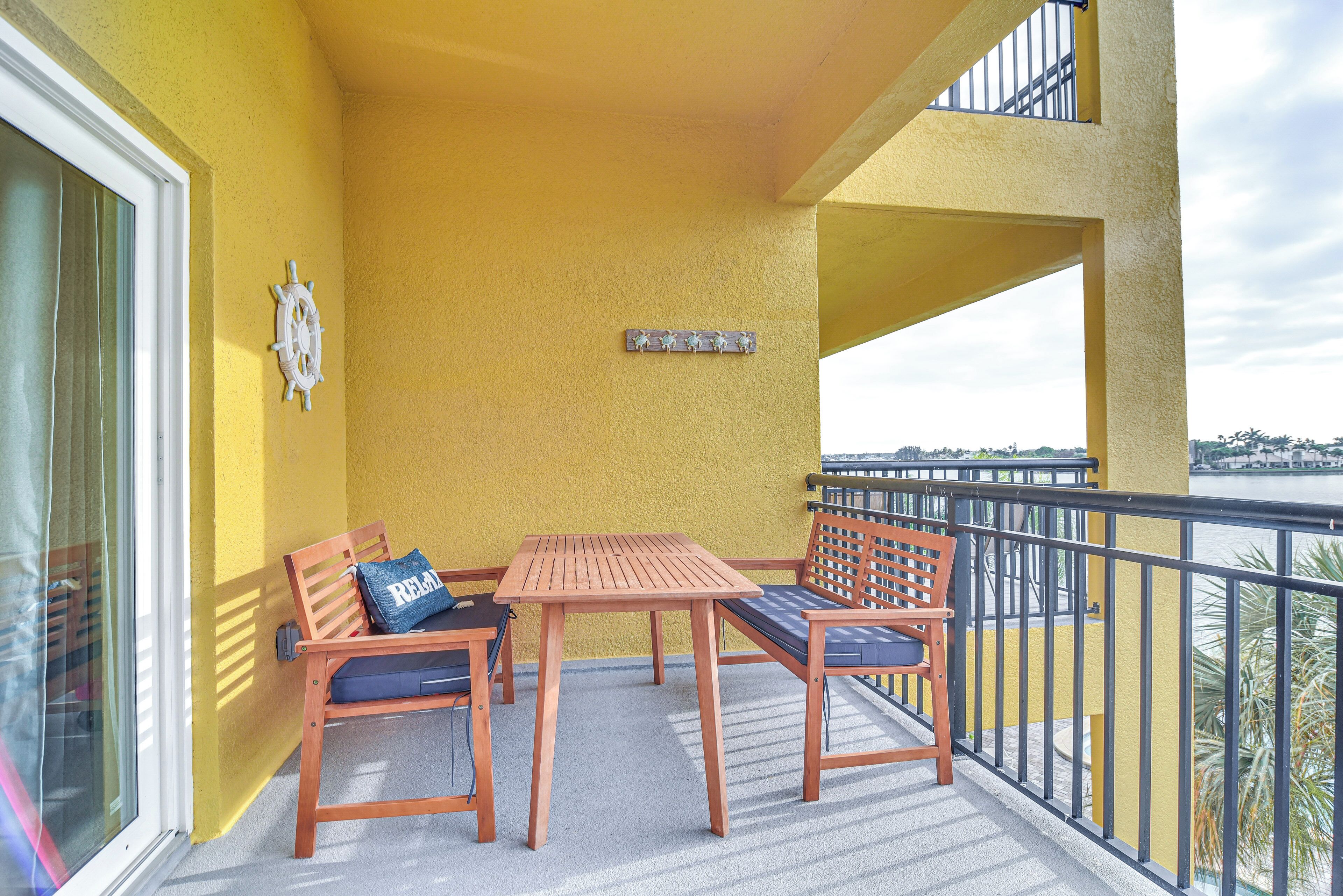 En balkon med gule vægge, et træbord, to stole og en dekorativt rat fra et skib.
