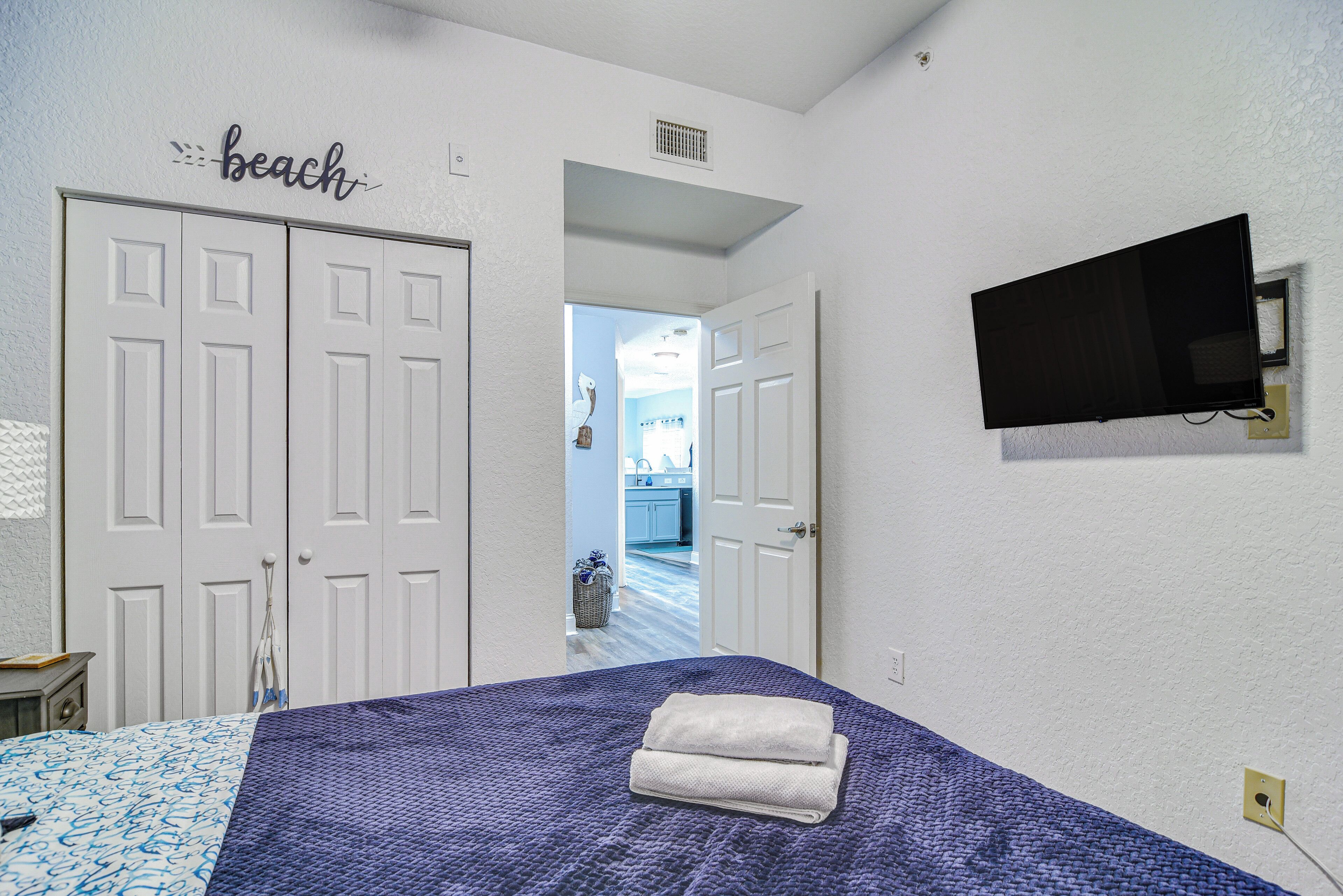 A bedroom with a bed, a TV mounted on the wall, and a door leading to a bathroom.