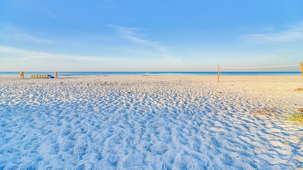 Une plage avec un filet de volley-ball, du sable et un ciel dégagé.