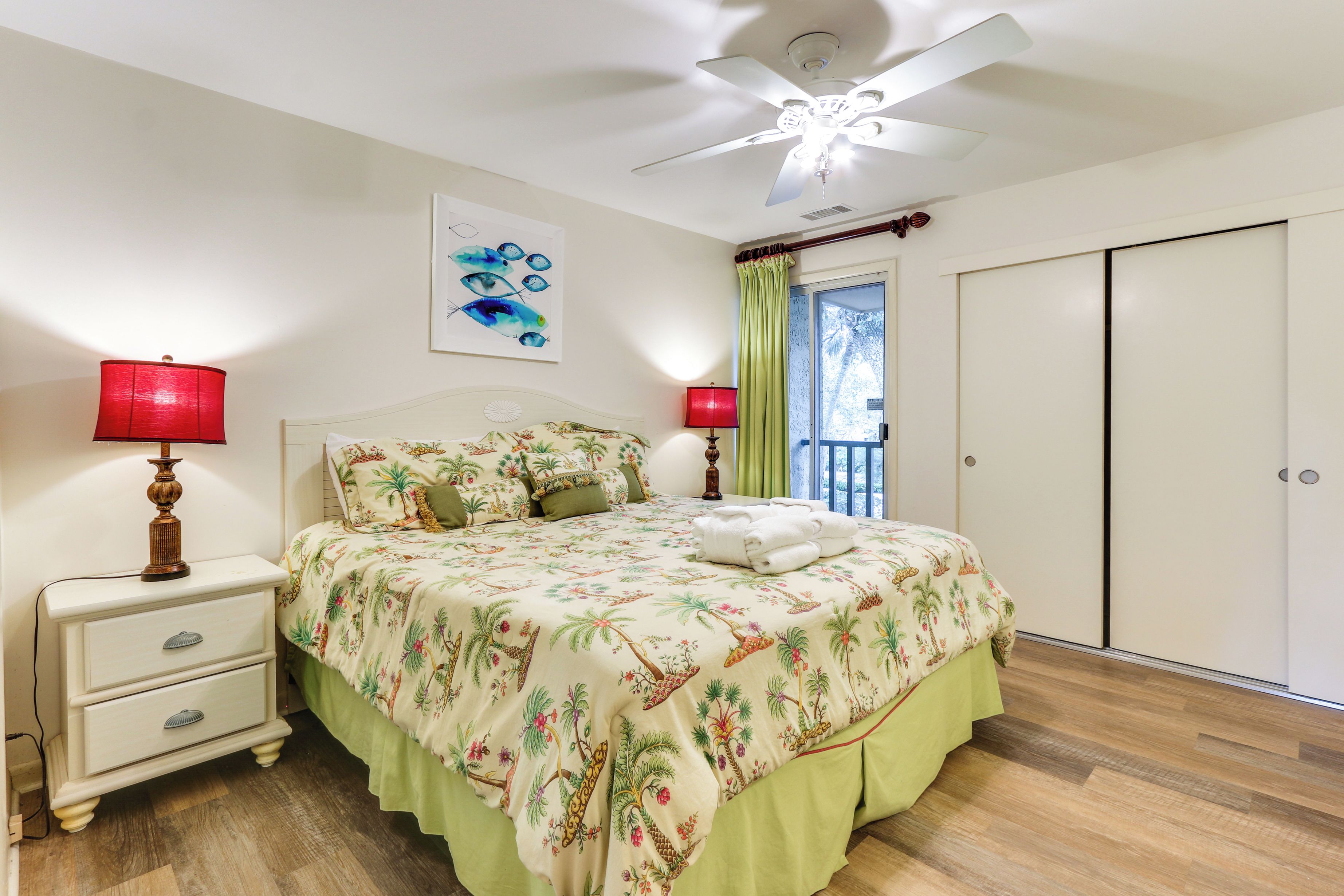A bedroom with a bed, nightstands, a ceiling fan, a window with curtains, and a door.
